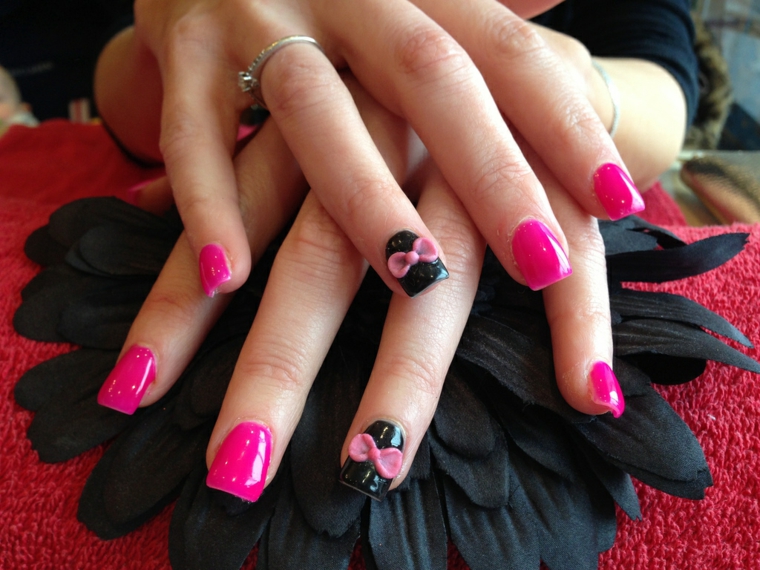 smalto rosa, una manicure realizzata con il gel con l'anulare nero decorato con un fiocco